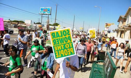 A group of people marching with a sign that reads "Solar power to the people."